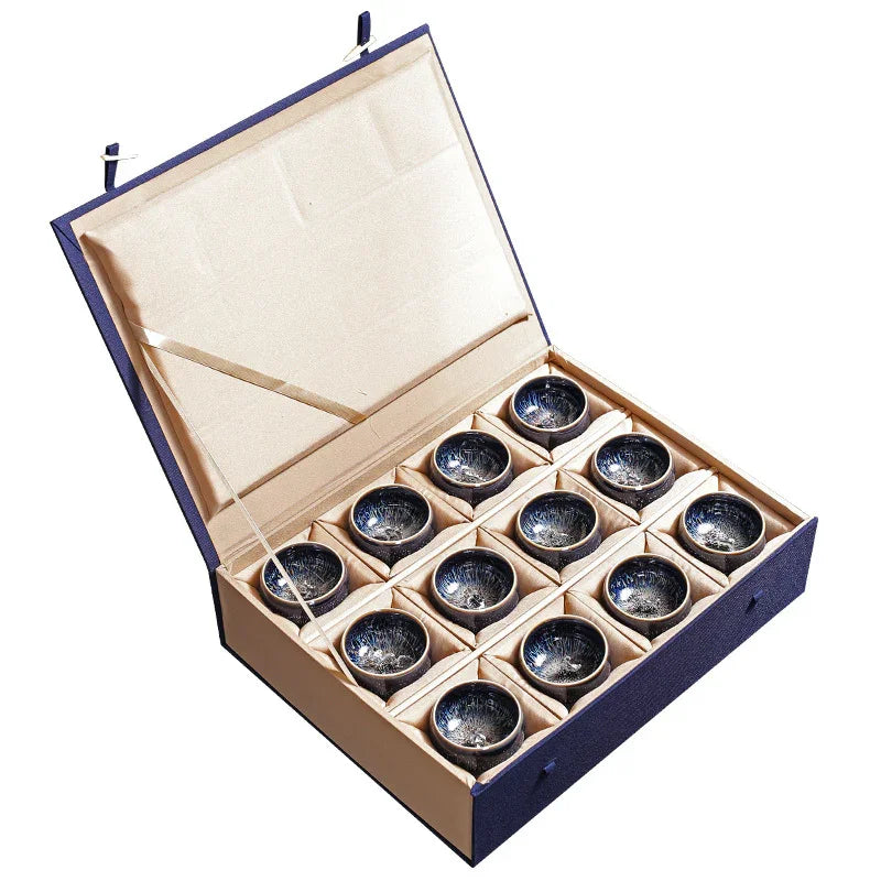 Open gift box containing 12 ceramic tea cups with dark blue glaze and intricate patterns