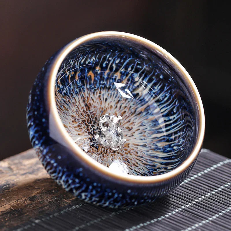 Blue ceramic bowl with intricate patterns and small silver frog figurine inside on wooden surface