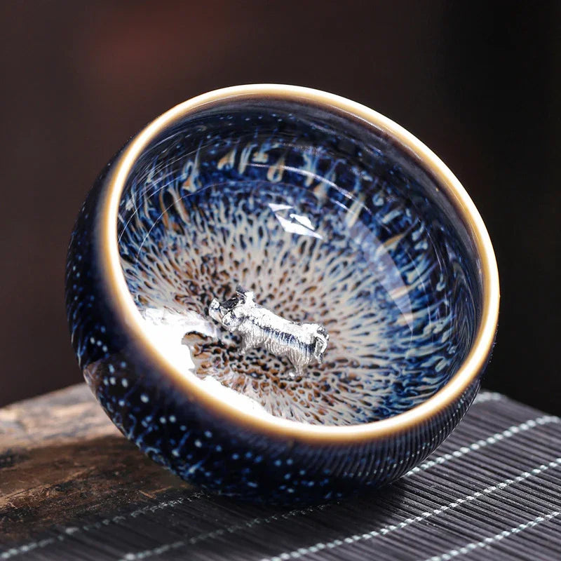 Blue ceramic bowl with intricate speckled glaze and silver bull figurine inside, on wooden surface