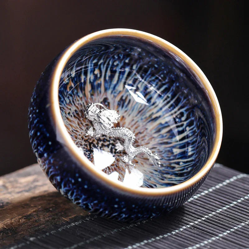 Blue ceramic bowl with intricate glaze and silver dragon ornament inside on wooden surface
