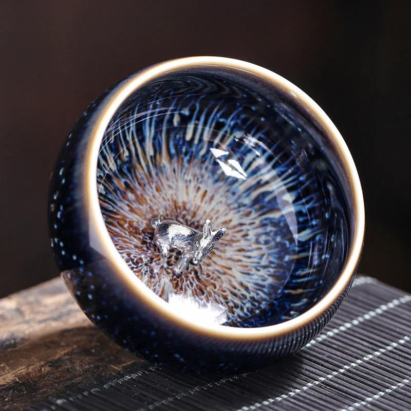 Close-up of a dark blue ceramic cup with a silver deer figurine inside and intricate radial patterns