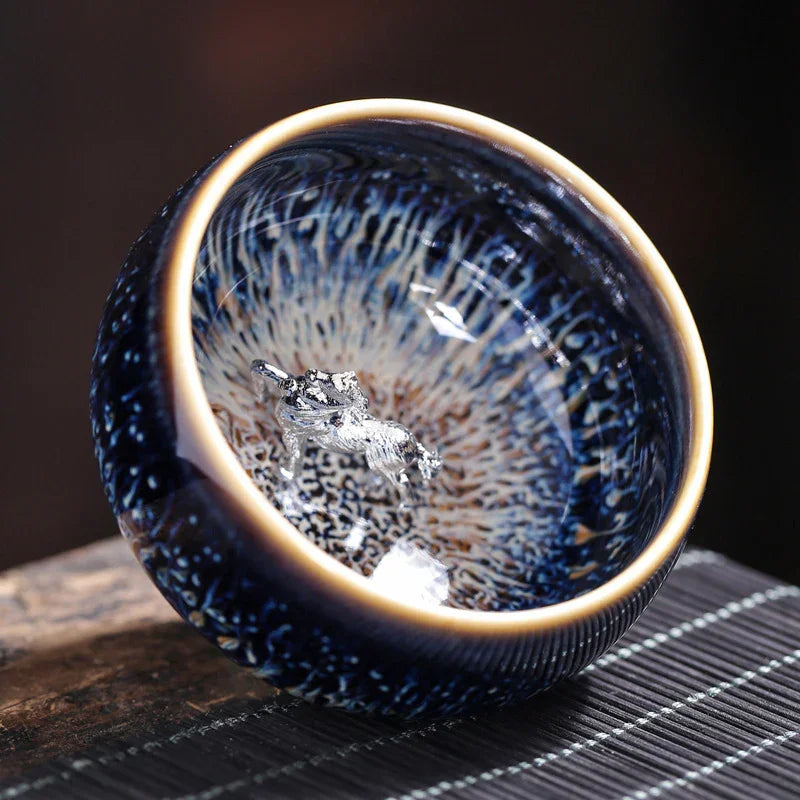 Close-up of a blue ceramic tea cup with intricate patterns and a silver dragon figure inside