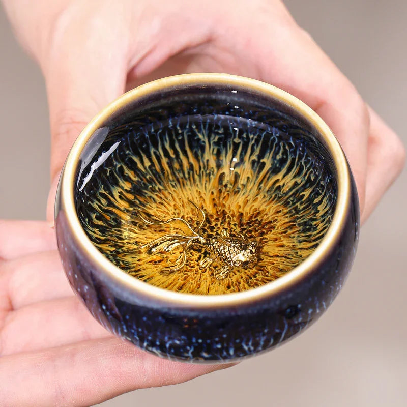 Hand holding a ceramic tea cup with golden fish design and unique textured glaze inside