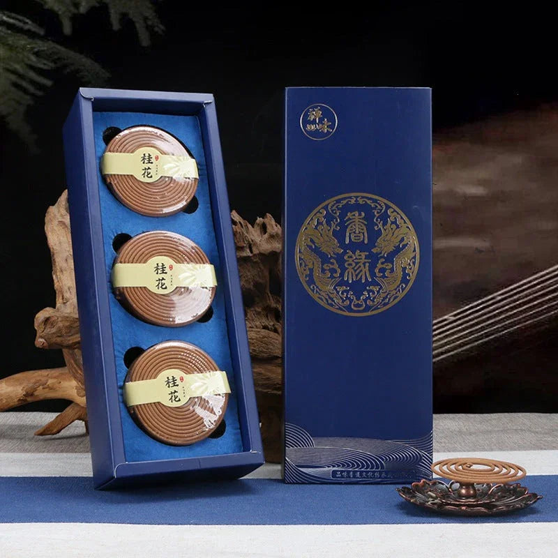 Blue box with three brown spiral incense coils and a bronze holder on a blue and white cloth