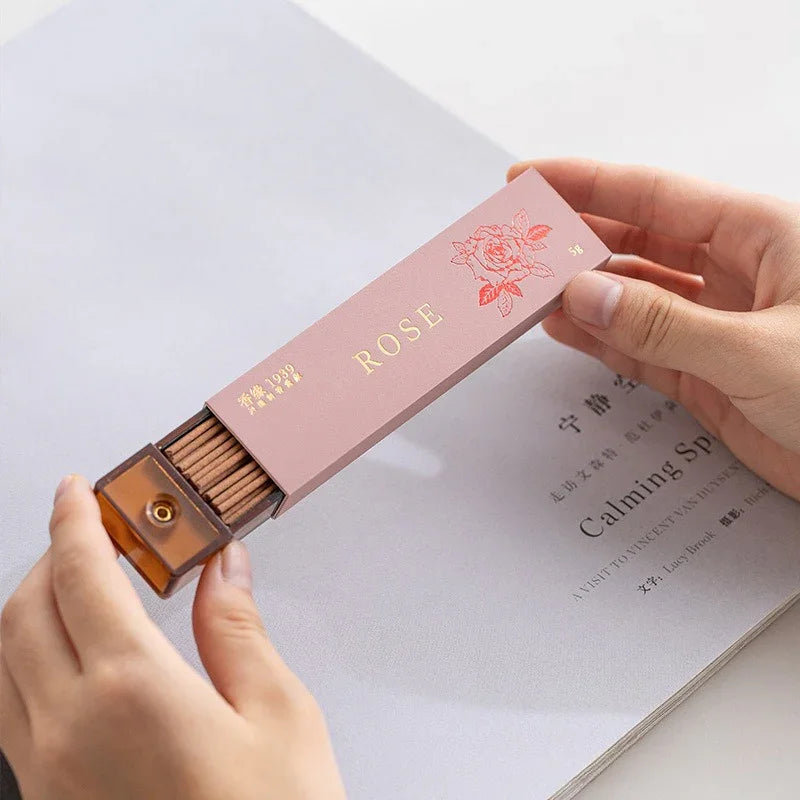 Hands holding pink box of rose scented incense sticks with floral design on light background