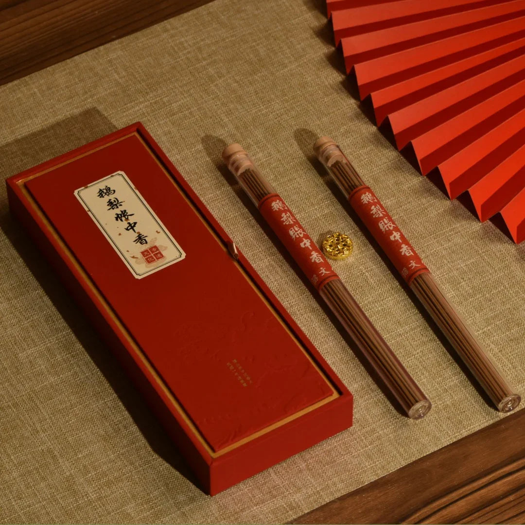 Red box and tubes of traditional Chinese incense sticks on beige fabric with a red decorative fan