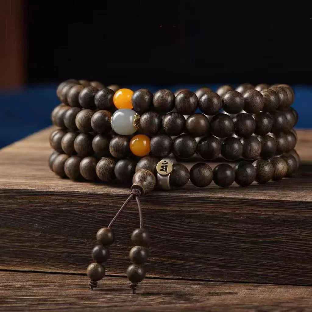 Close-up of dark wooden mala prayer beads with yellow and white accent beads on rustic wooden surface