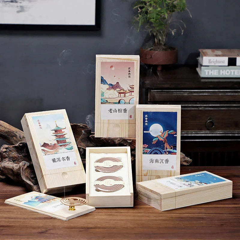 Wooden boxes of traditional Chinese incense coils with artistic landscape and bird illustrations on labels, emitting smoke