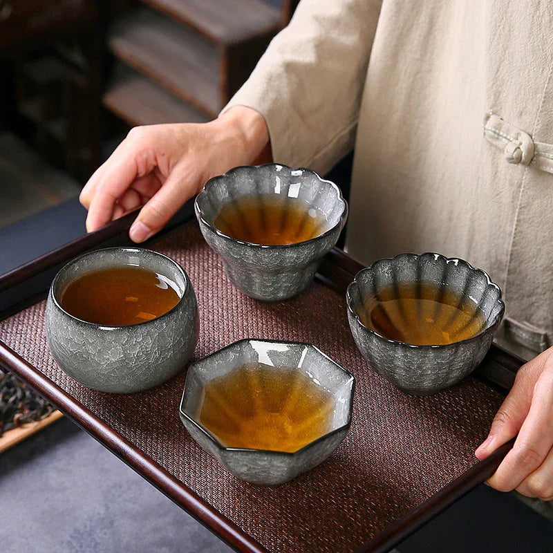 Person holding wooden tray with four textured ceramic tea cups filled with amber tea