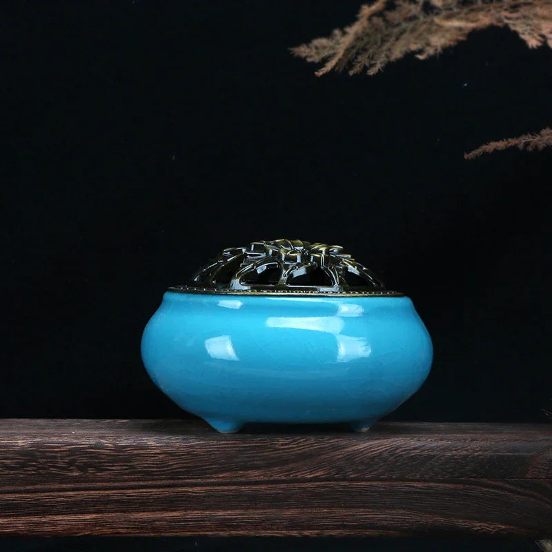 Blue ceramic incense burner with ornate metal lid on wooden surface, black background