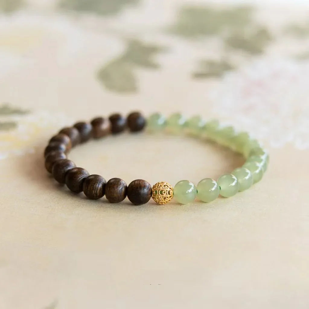 Beaded bracelet with dark wood, green jade beads, and a decorative gold bead on beige background