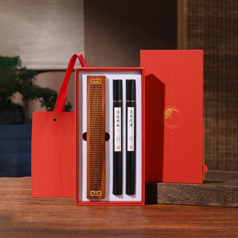 Red gift box with two black incense sticks and a wooden incense holder on a wooden table