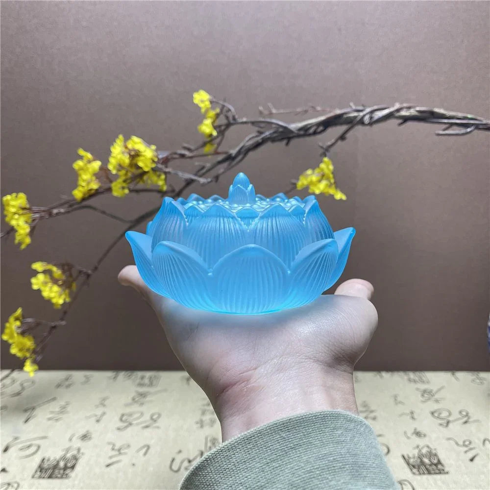 Hand holding a translucent blue lotus-shaped candle holder with yellow flowers and calligraphy background