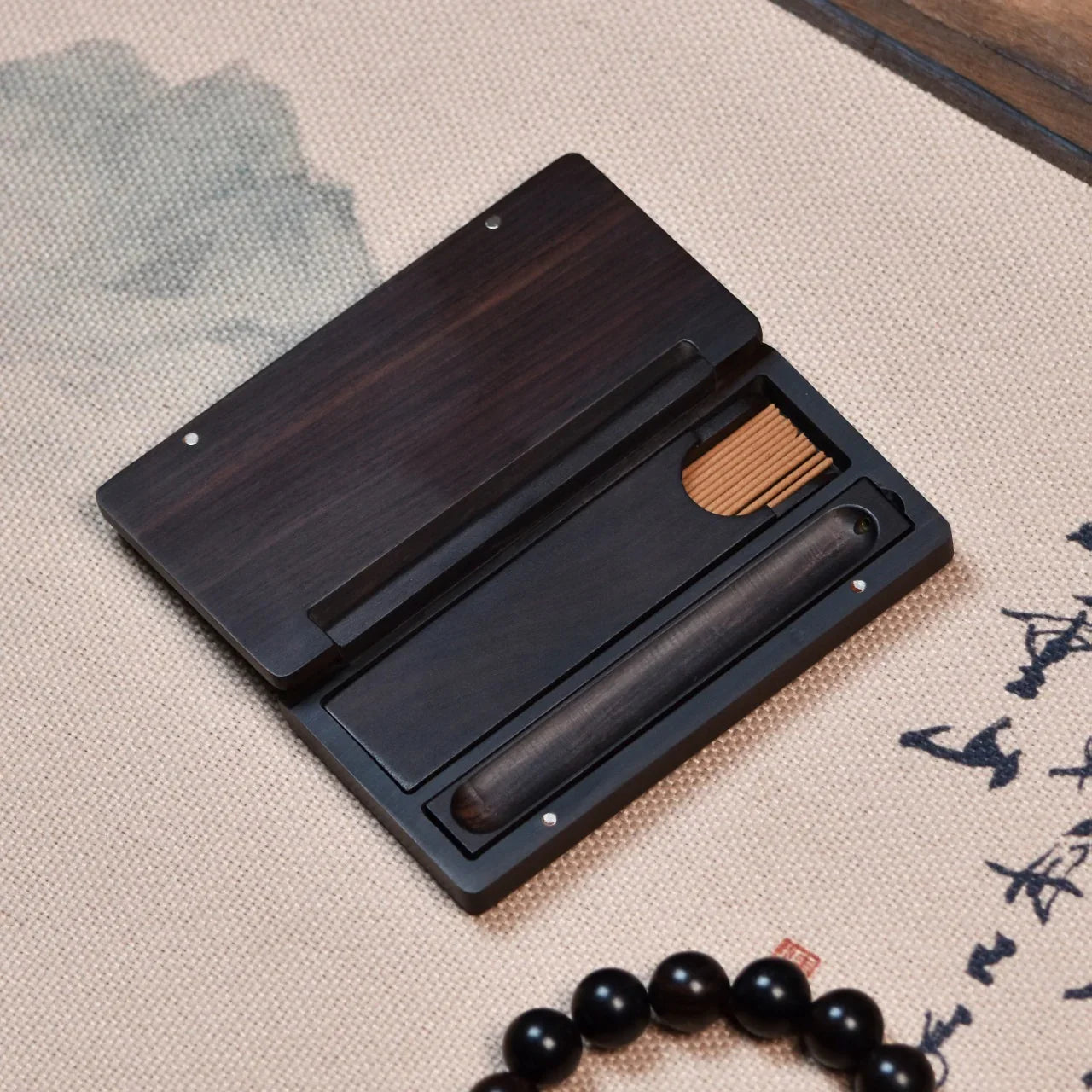 Dark wooden incense holder box with sticks on beige fabric with calligraphy and black bead bracelet