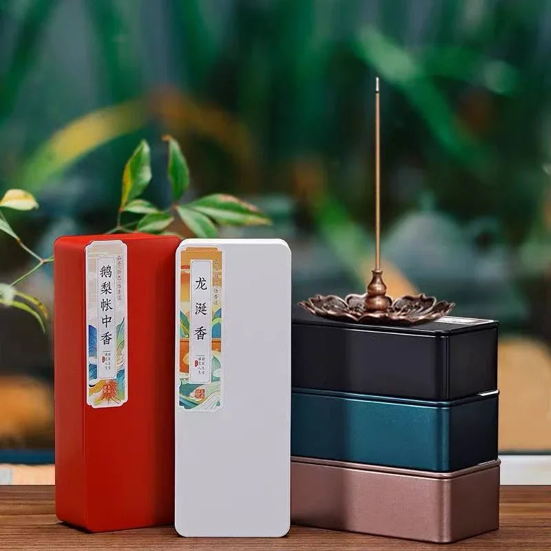 Elegant incense boxes in red and white with Chinese labels, stacked metallic tins, and a lit incense stick in a lotus holder