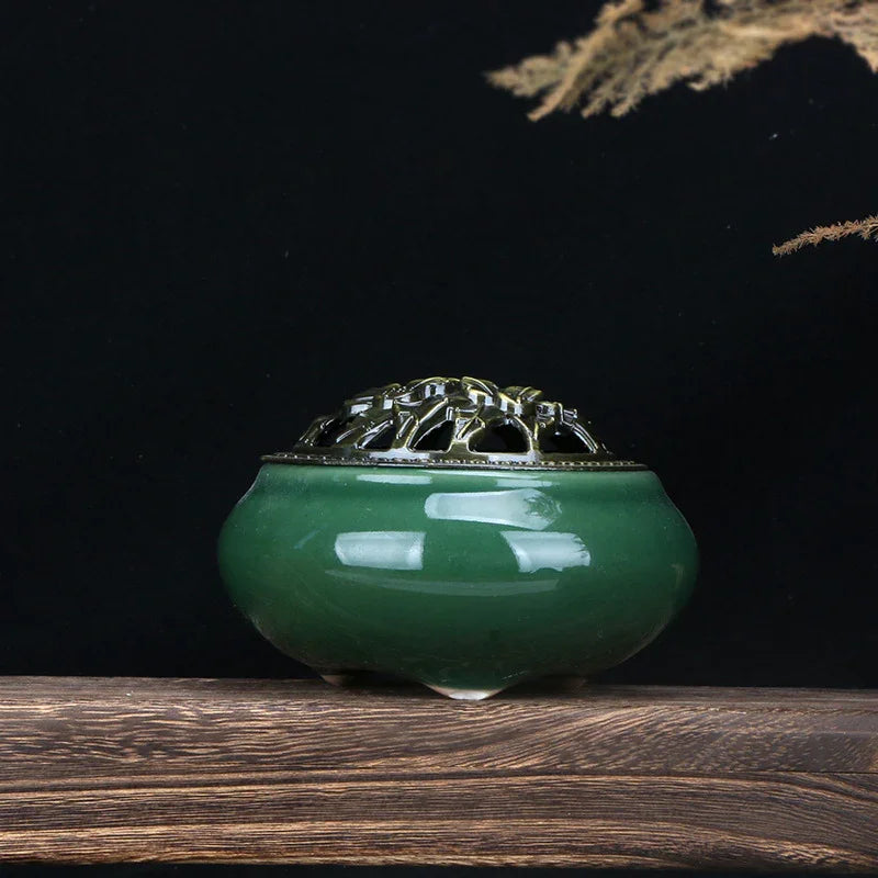 Green ceramic incense burner with intricate metal lid on wooden surface against black background