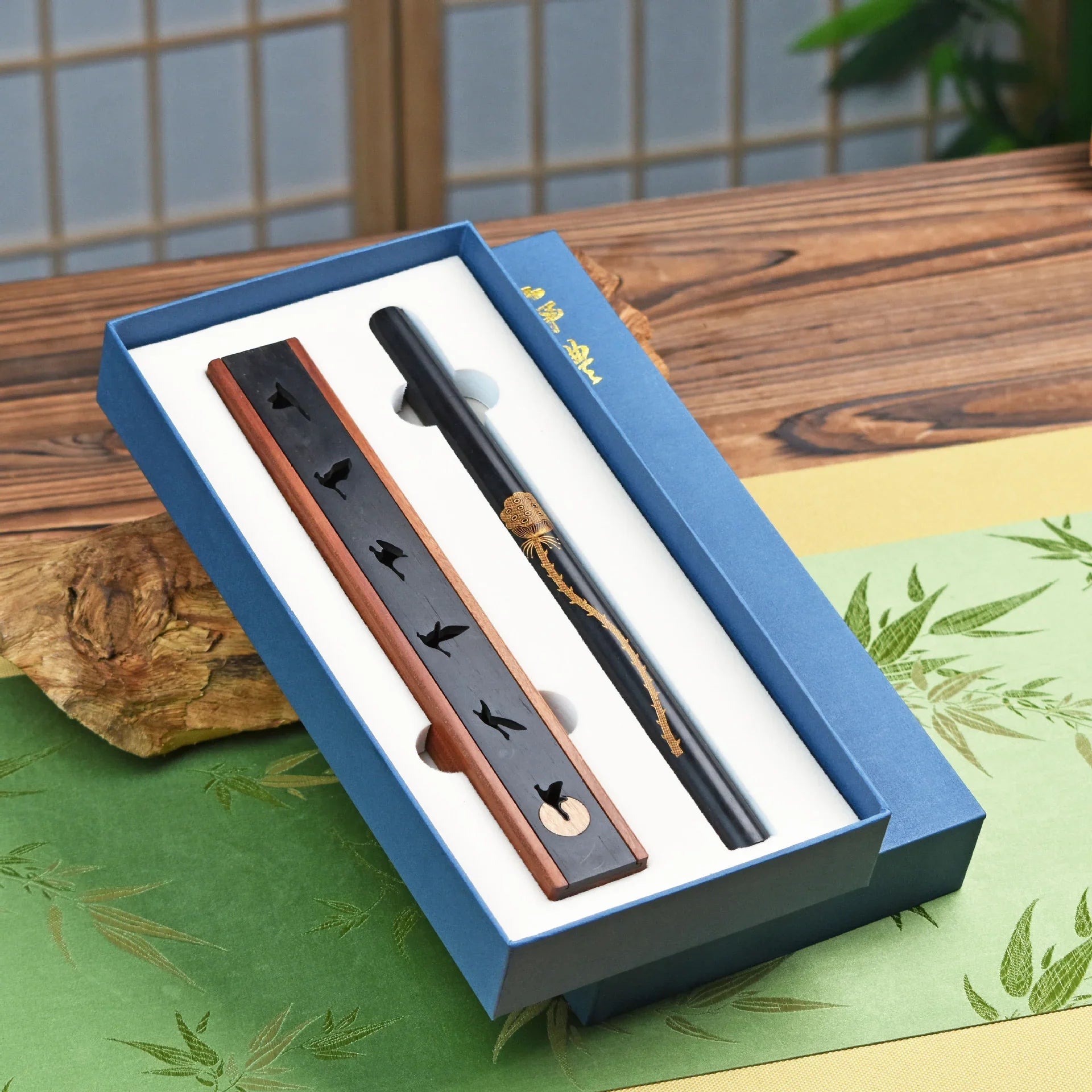 Traditional black incense holder with bird cutouts and decorative incense stick in blue gift box on wooden table
