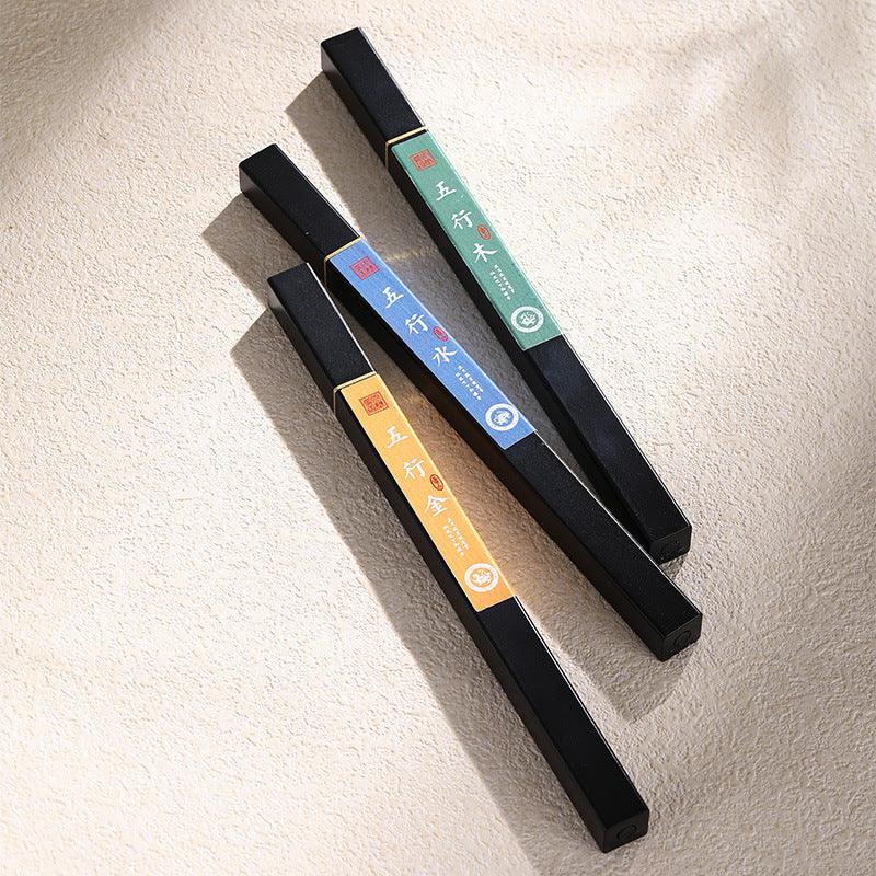 Three rectangular black incense boxes with colorful labels in green, blue, and yellow featuring Chinese characters, on textured beige surface