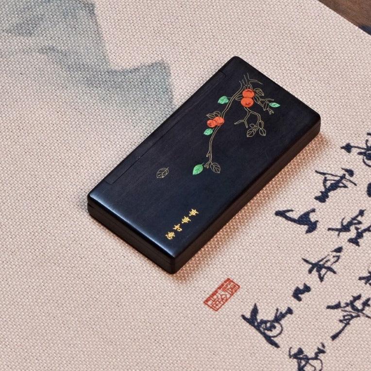 black rectangular box with decorative floral branch and gold Chinese characters on textured fabric with calligraphy