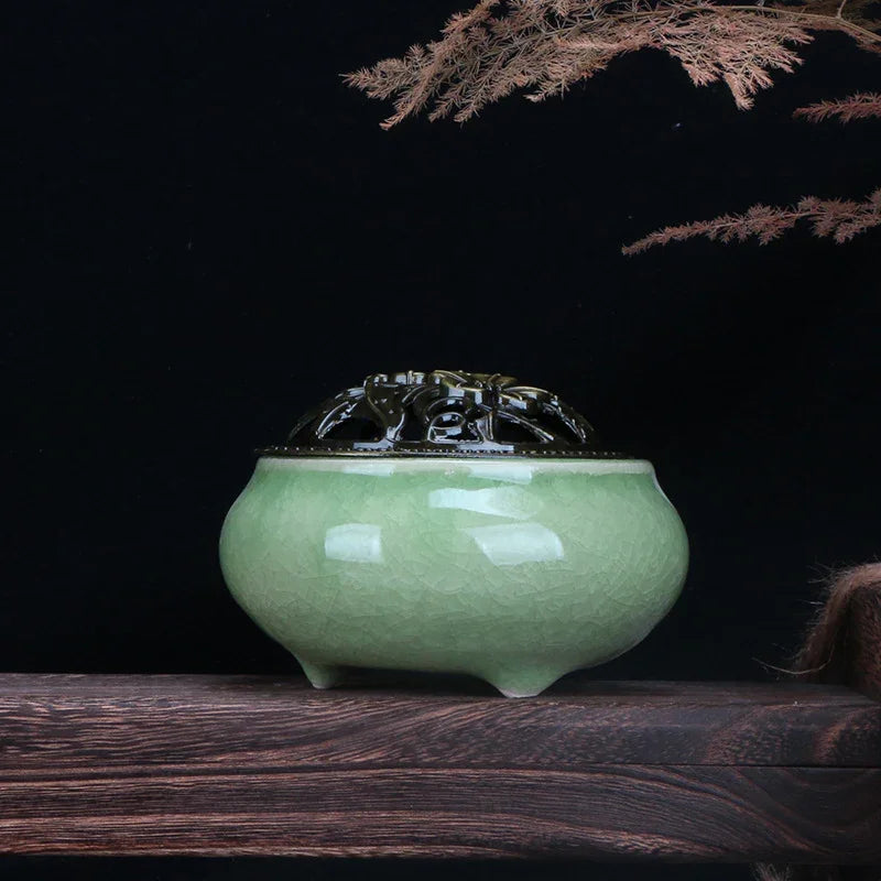 Green ceramic incense burner with metal lid on dark wooden table against black background