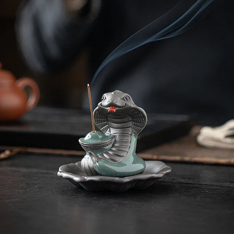 Ceramic cobra incense holder with burning incense stick and rising smoke on dark surface