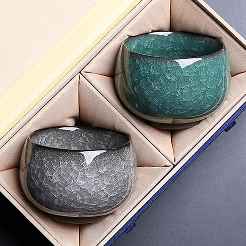 Set of two textured ceramic cups in grey and green, elegantly placed in a beige padded gift box