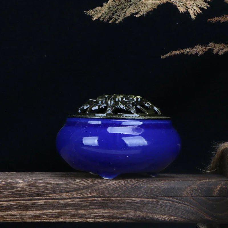 Blue ceramic incense burner with ornate brass lid on wooden surface against black background