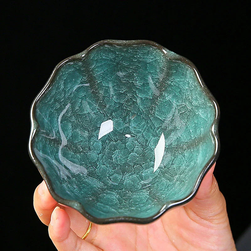 Hand holding a small scalloped turquoise ceramic bowl with textured crackle glaze