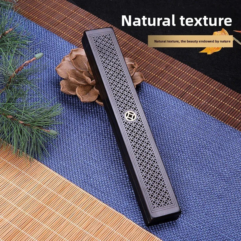 Decorative long rectangular wooden incense holder with intricate pattern on textured fabric mat and pine branch