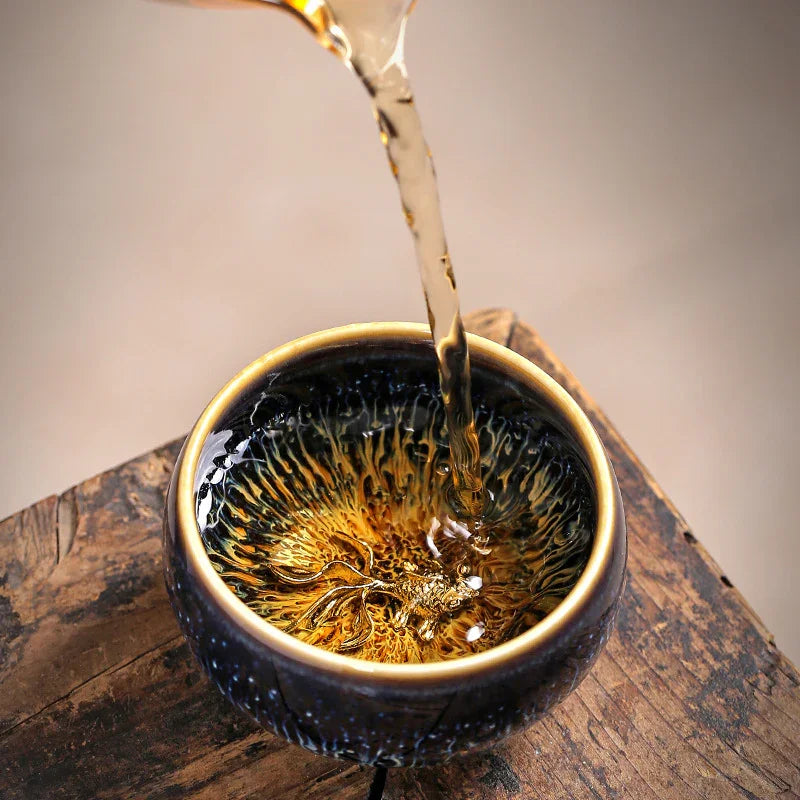 Pouring tea into a dark ceramic cup with a detailed golden dragon design inside on wooden surface