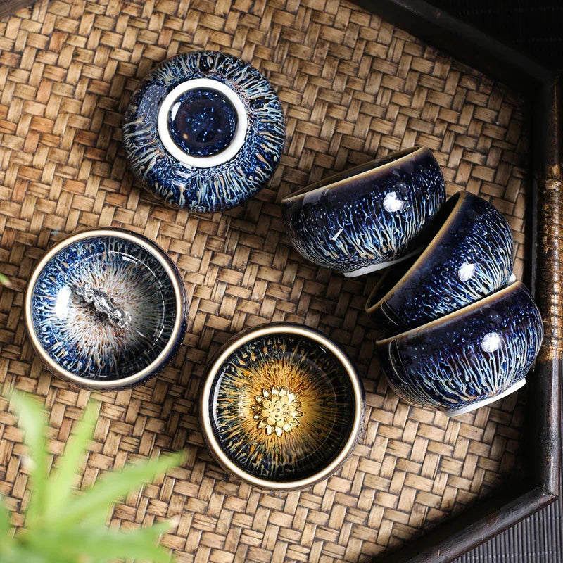 Set of blue and brown ceramic tea cups with intricate glaze patterns on a woven bamboo tray