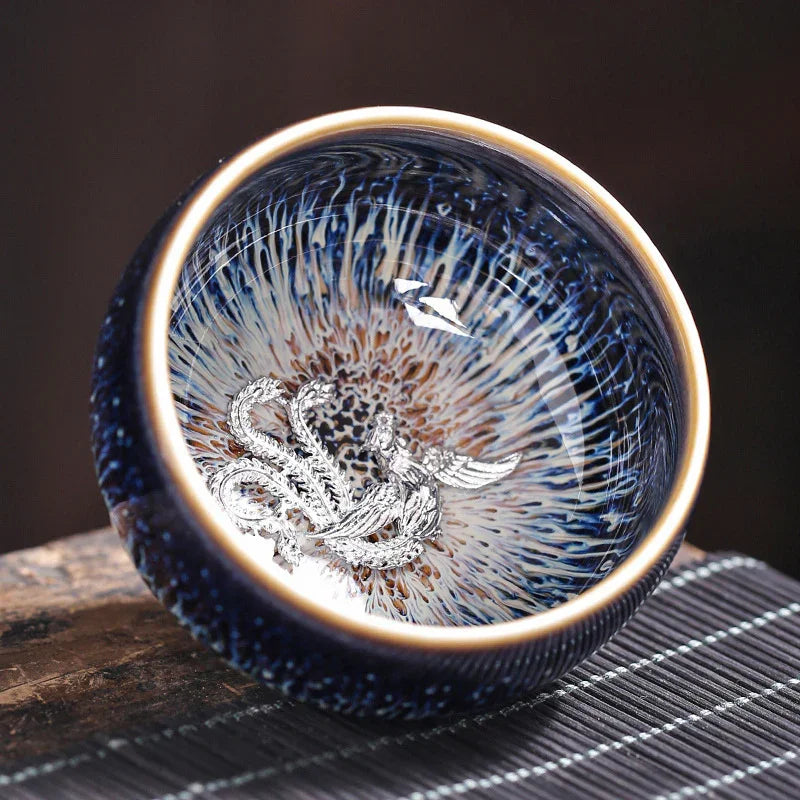 Ceramic tea bowl with intricate blue and brown glaze and silver dragon design inside, placed on wooden surface