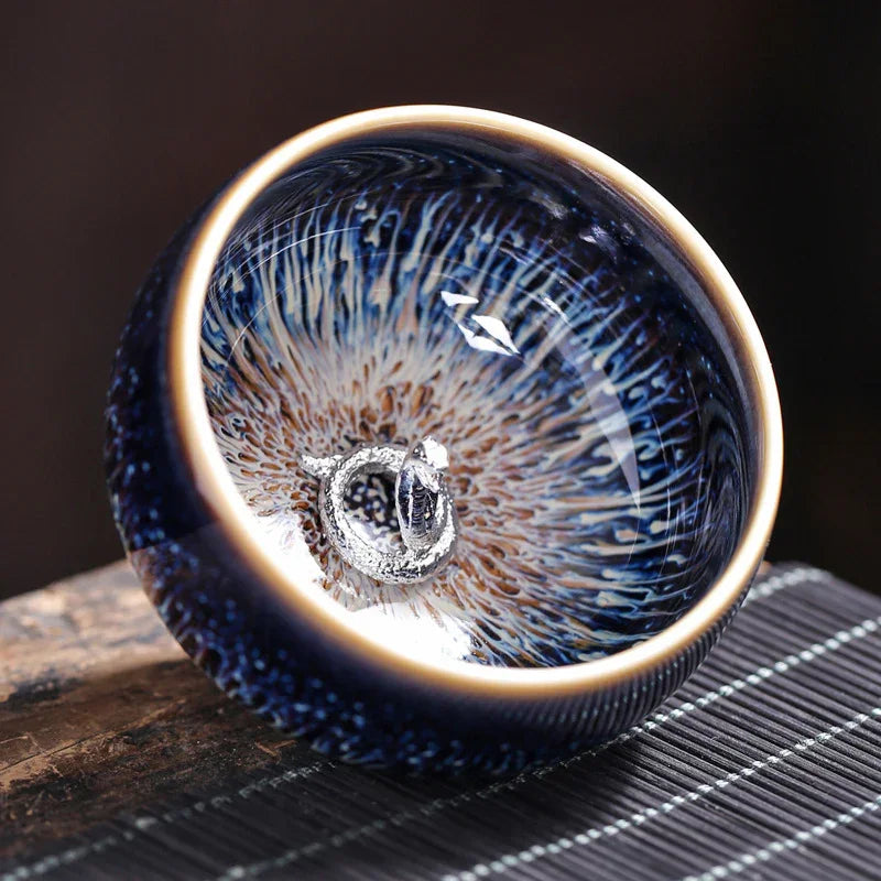 Close-up of a dark blue ceramic tea bowl with intricate glaze pattern and silver dragon detail inside