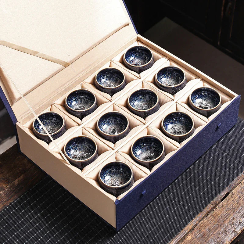 Set of twelve black ceramic tea cups with intricate blue and white inside glaze, neatly packed in a beige and navy gift box