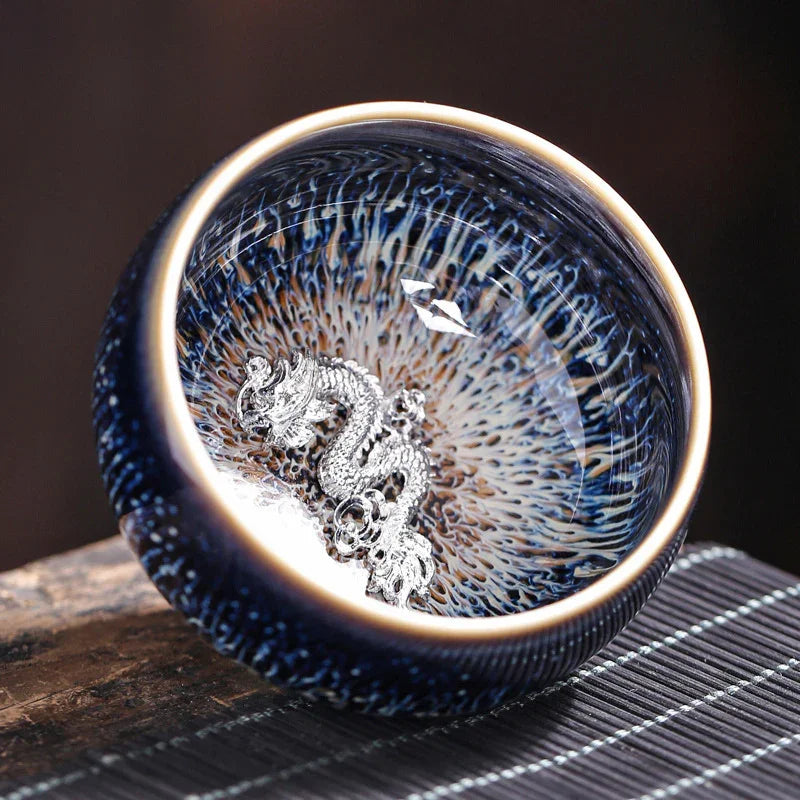 Blue ceramic bowl with intricate silver dragon inside on wooden surface and bamboo mat