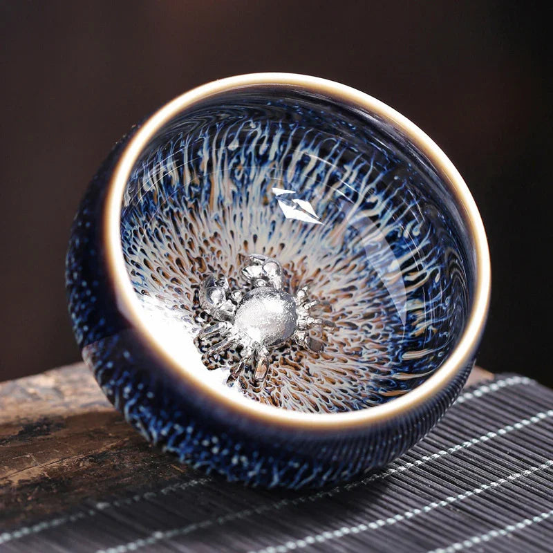 Blue ceramic bowl with textured exterior and metallic silver crab decoration inside on wooden surface