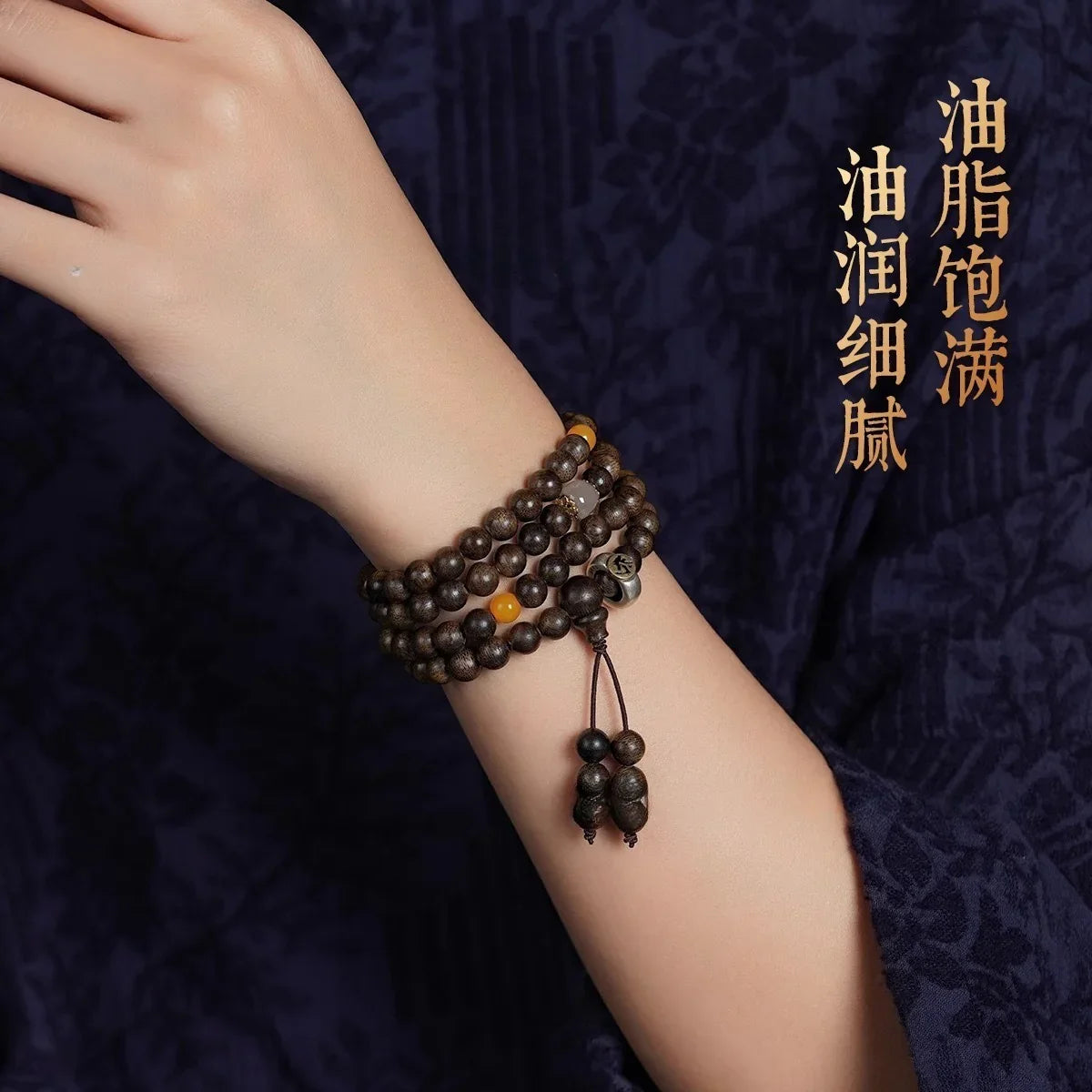 Closeup of hand wearing dark brown wooden bead bracelet with yellow and gray beads on dark floral fabric background