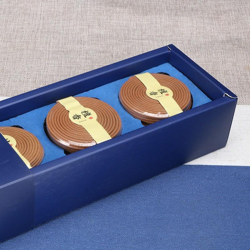 Blue gift box with three round brown incense coils in transparent lids and yellow labels on blue fabric
