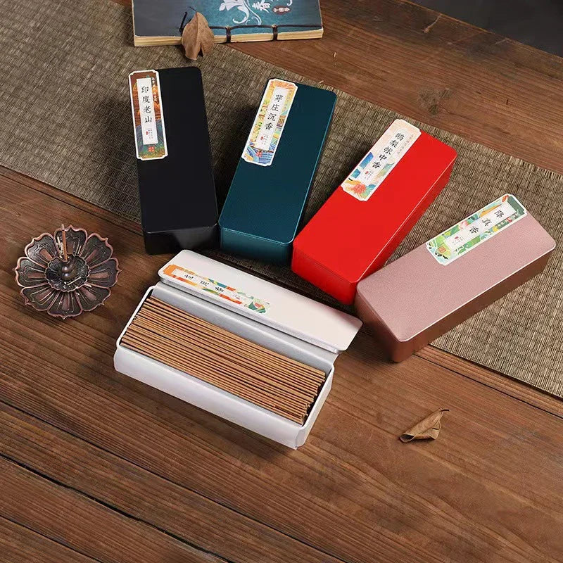 Colorful rectangular incense stick boxes arranged on a wooden surface with a metal incense holder and dried leaves