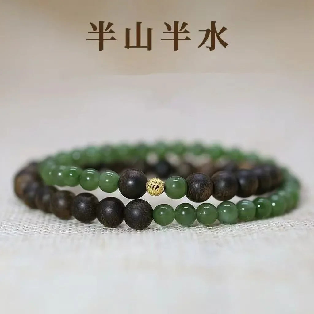 Close-up of green jade and dark wood bead bracelets with a gold decorative bead on neutral fabric
