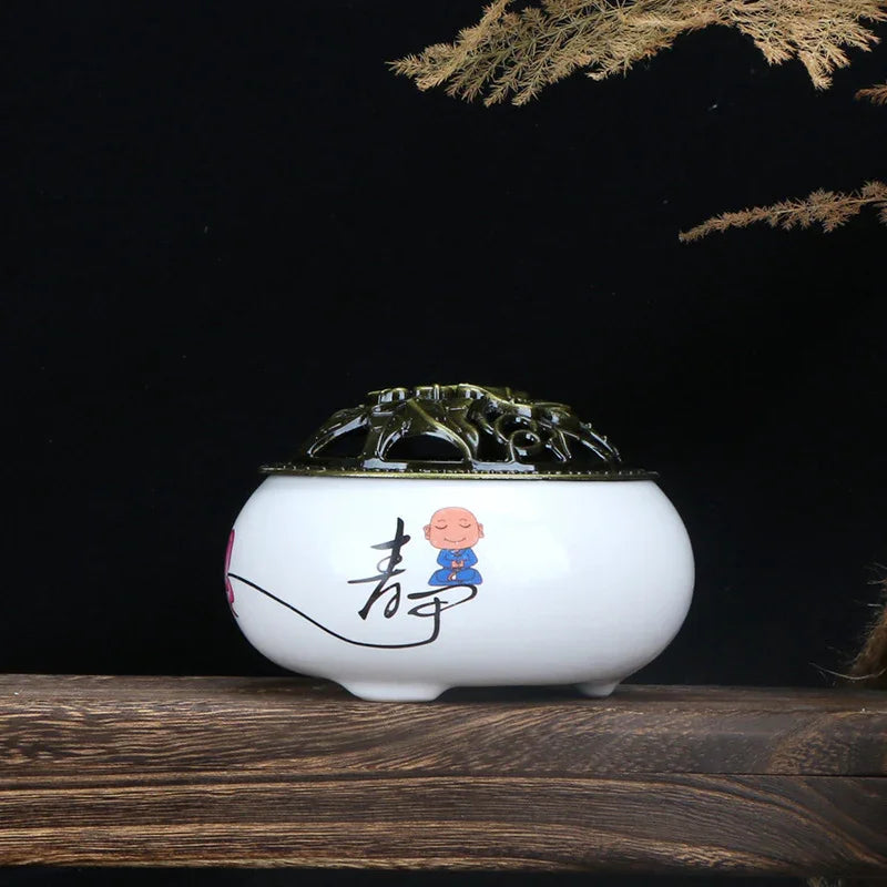 White ceramic incense burner with black Chinese character and meditating monk illustration, wooden surface