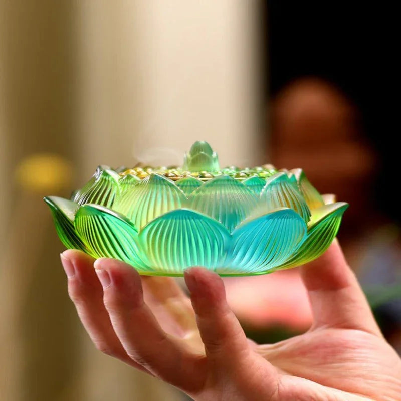 hand holding green and blue lotus-shaped glass incense burner with smoke