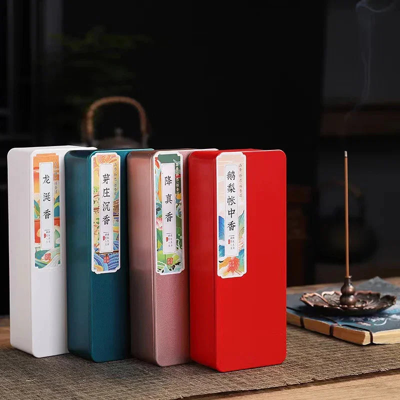 Colorful rectangular incense gift boxes displayed on a woven mat with a lit incense stick in a holder