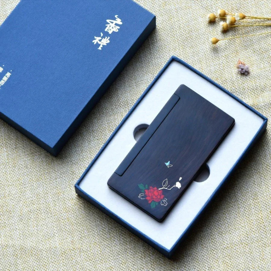 Elegant wooden card holder with floral and butterfly design in open blue gift box on textured fabric