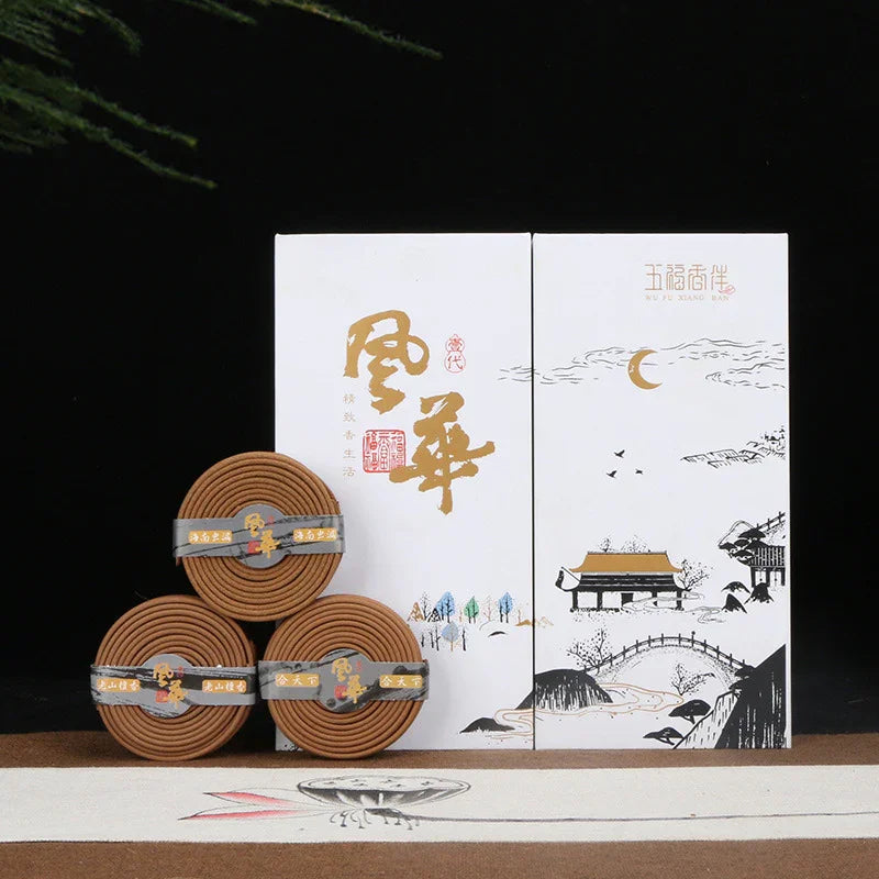 Three brown incense coil packs stacked beside white boxes with gold Chinese characters and traditional landscape art
