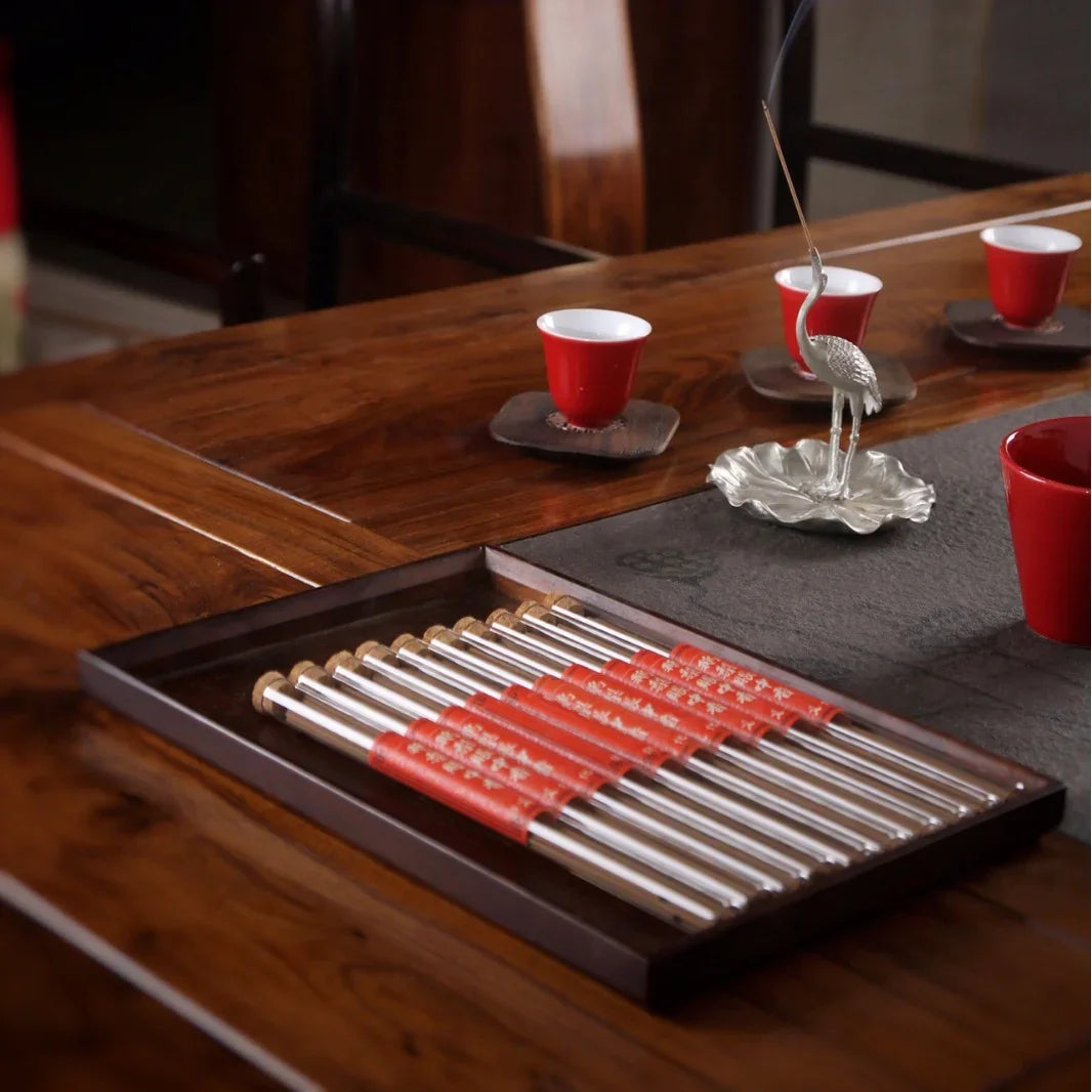 Chinese tea set on wooden table with silver incense holder and red chopsticks in tray