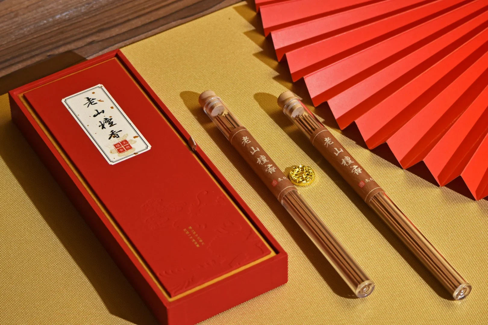 Red gift box with Chinese incense sticks in plastic tubes and a red folding fan on gold textured surface