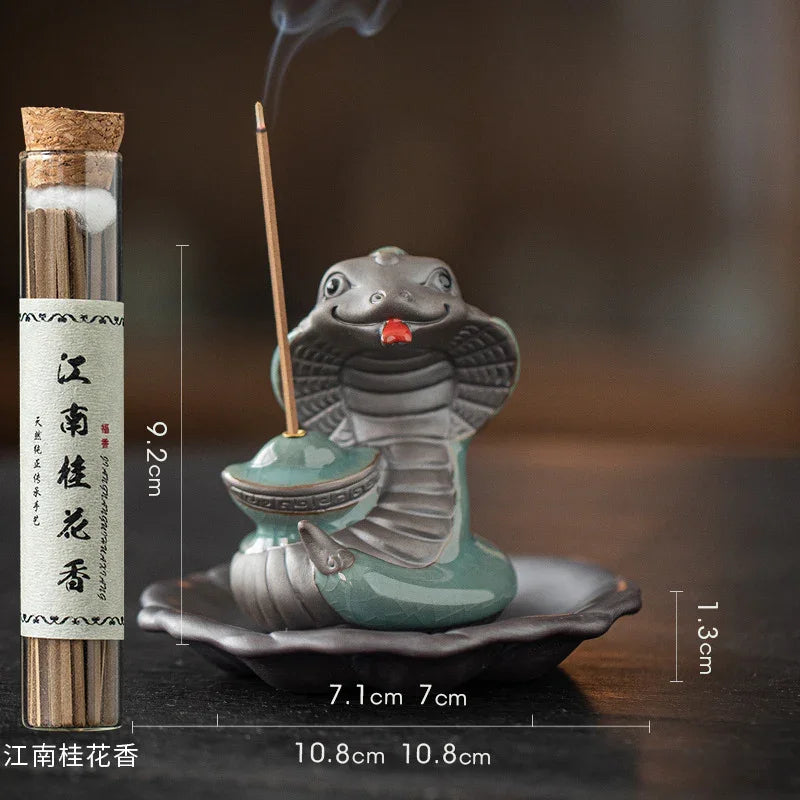 Ceramic cobra incense holder with burning stick next to jar of cinnamon incense sticks