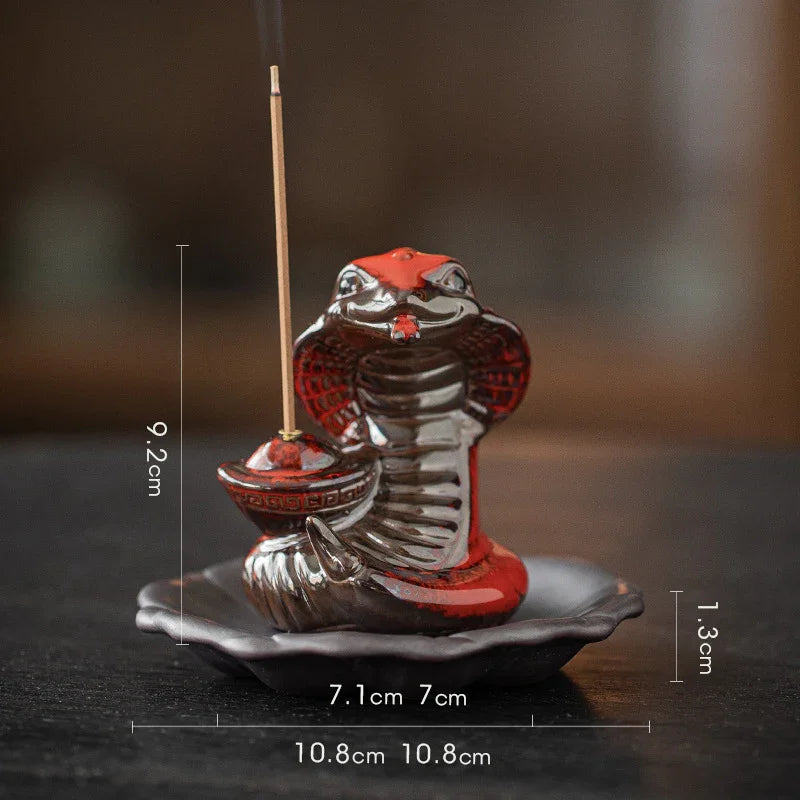 Red and black ceramic cobra incense holder with measuring lines on dark surface
