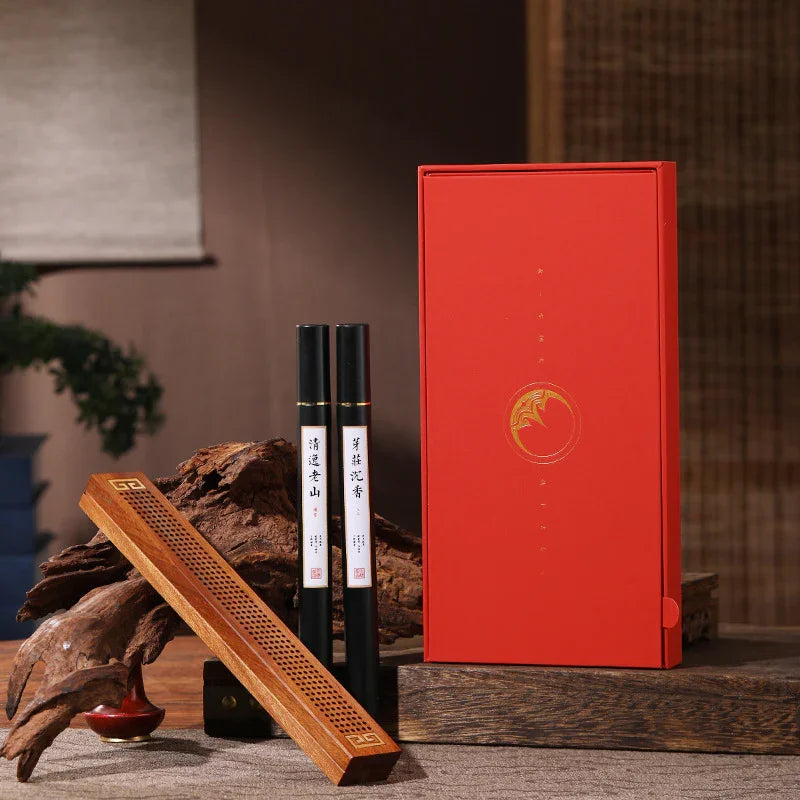 Red gift box with gold emblem, two black incense holders, and wooden incense burner on wooden surface